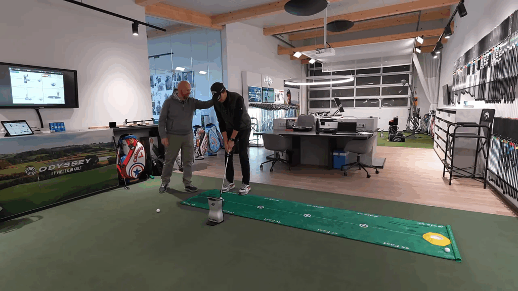 Fitter justiert die Körperhaltung des Spielers beim Putting‑Setup, Fokus auf Augenlinie und Ballposition