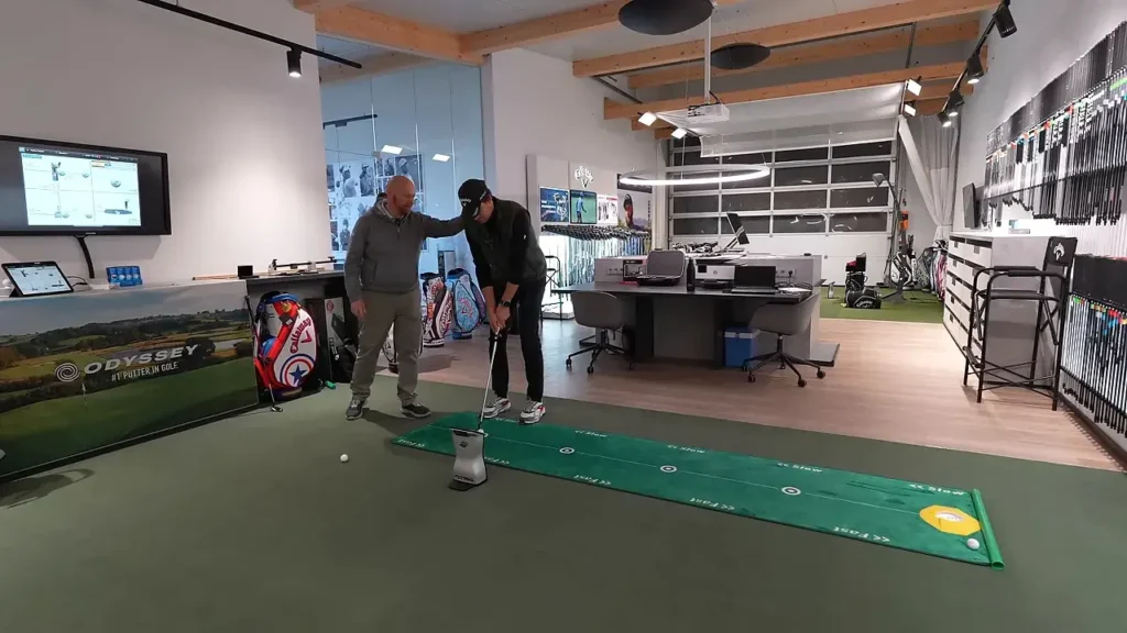 Fitter justiert die Körperhaltung des Spielers beim Putting‑Setup, Fokus auf Augenlinie und Ballposition