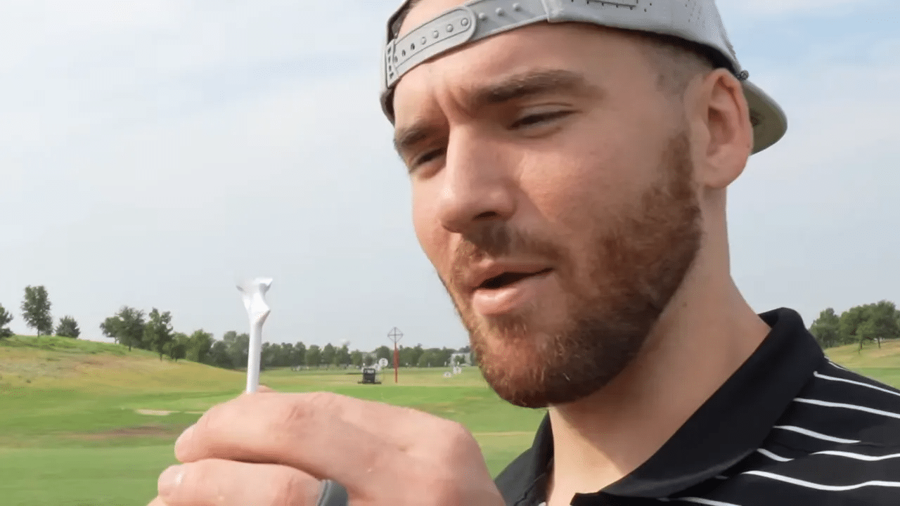 Nahaufnahme eines weißen Golf-Tees in der Hand vor der Driving Range