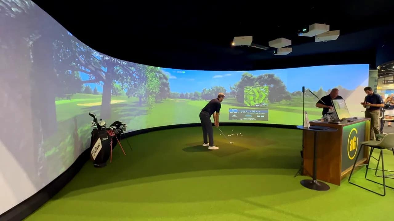 Wide curved aboutGOLF simulator installation with green turf, player at the tee and multiple projectors overhead.