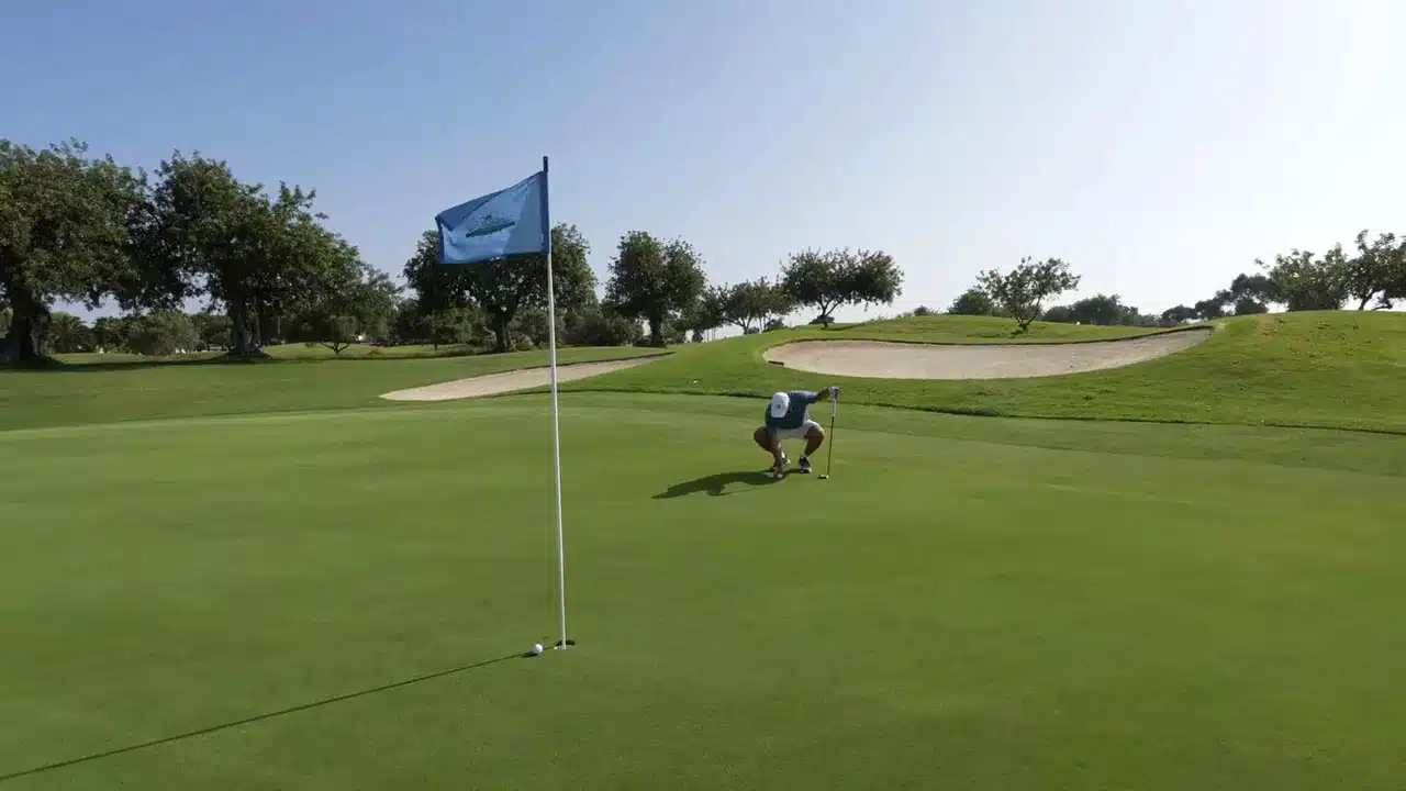 Quinta da Ria Golfplatz: Golfen am Atlantik, Familie und ein Match mit dem Clubdirektor 1 Grün mit Fahne und Golfball, Spieler liest den Putt; Bunker und Bäume im Hintergrund auf dem Quinta da Ria Golfplatz.