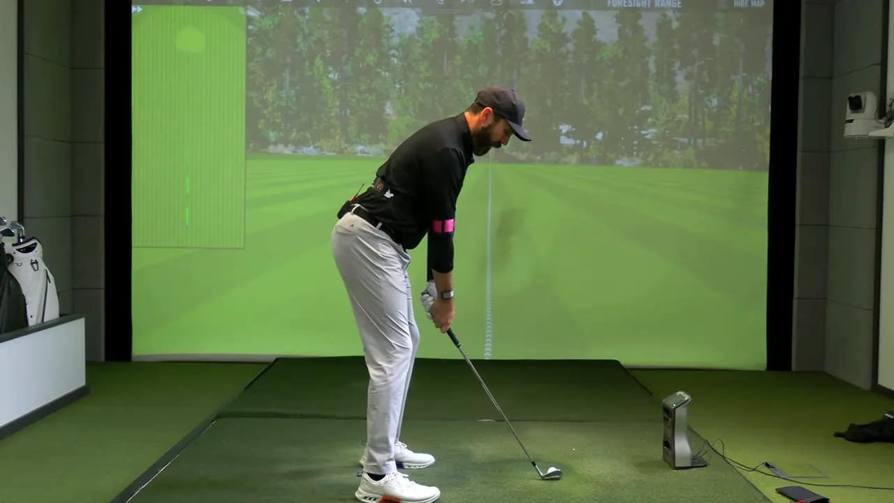 Golfer im Indoor-Simulator in der Ansprechposition mit pinkem TRS Slider am rechten Oberarm