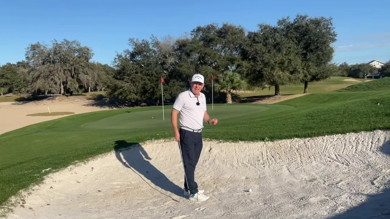 Golfspieler im Bunker zeigt zur Trefferzone neben dem Ball