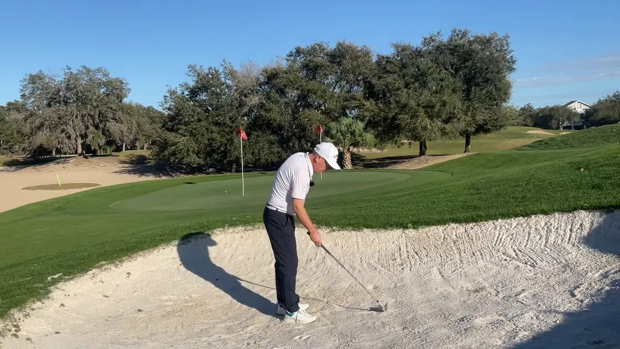 Golfspieler startet einen kurzen Bunkerschlag mit Fokus auf Erstkontakt im Sand